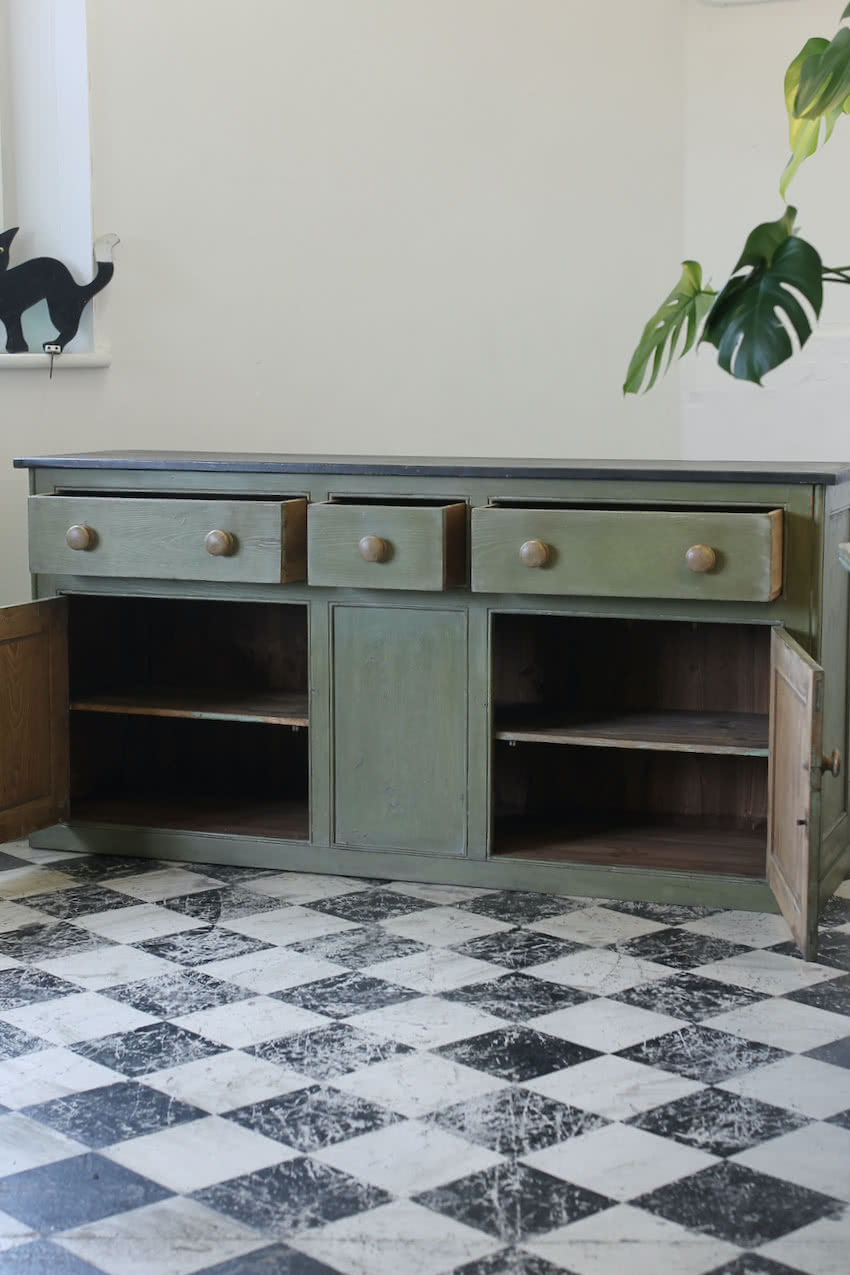 restored english three drawer cupboard base with contrasting large wooden knobs and interior pine shelf and black top.