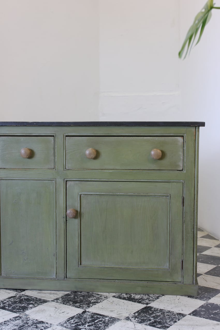 restored english three drawer cupboard base with contrasting large wooden knobs and interior pine shelf and black top.