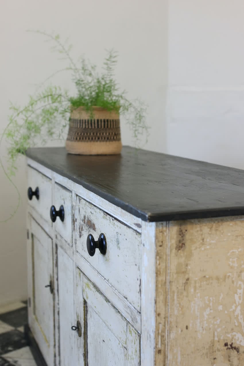 large english pine three drawer cupboard base hand scraped to reveal te old colours, the base has a black top, black wooden knobs and large round escutcheons.