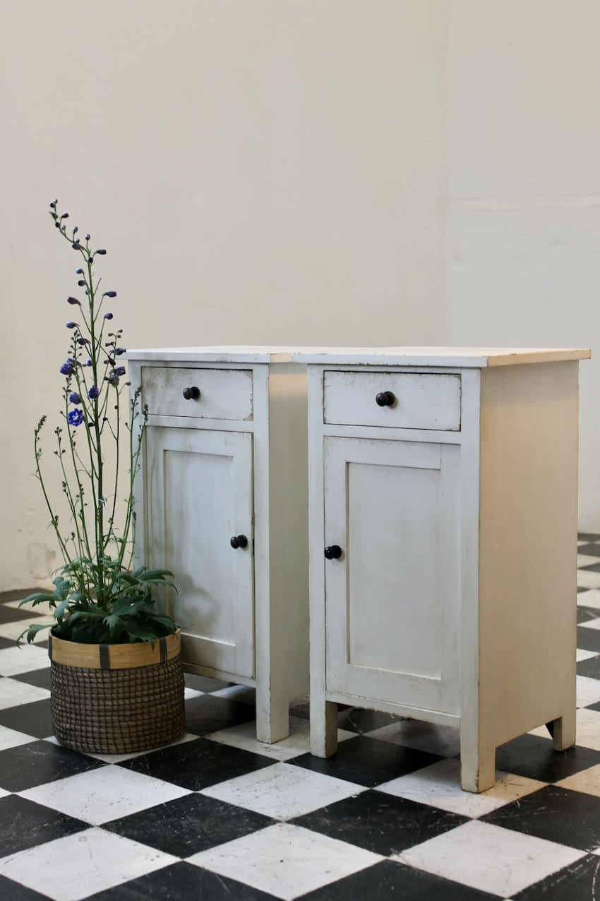 matching pair of painted white bedside cupboards with a drawer, small shelf inside, black wooden knobs and a painted interior.
