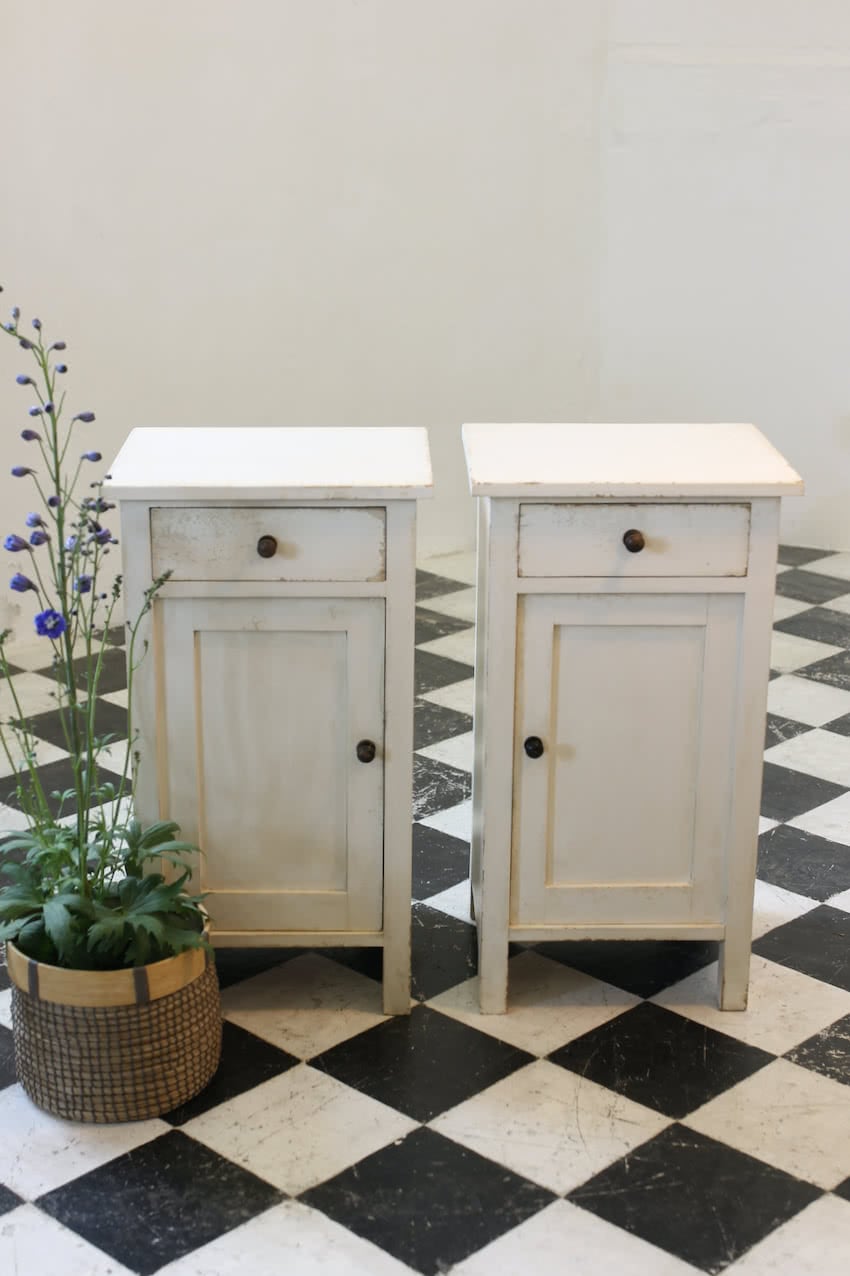 matching pair of painted white bedside cupboards with a drawer, small shelf inside, black wooden knobs and a painted interior.